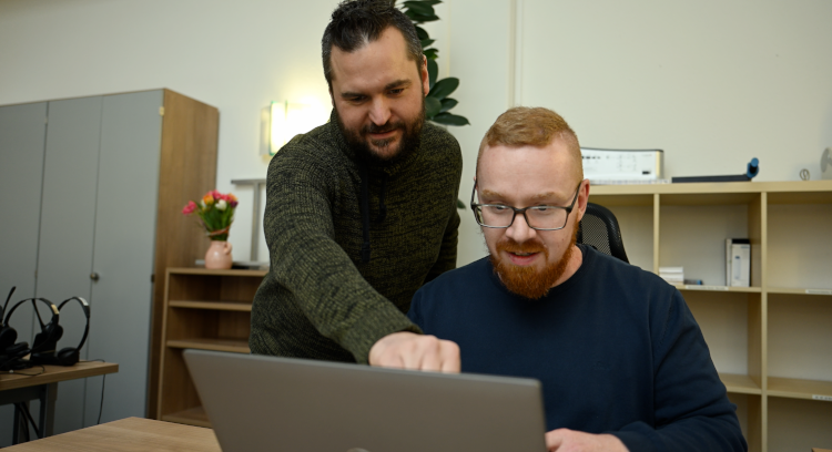 Zwei Männer sitzen am Laptop und diskutieren.