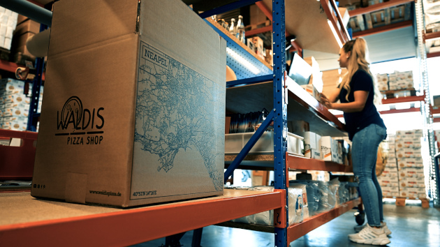 Karton und junge Frau im Lager von Waldis Pizza
