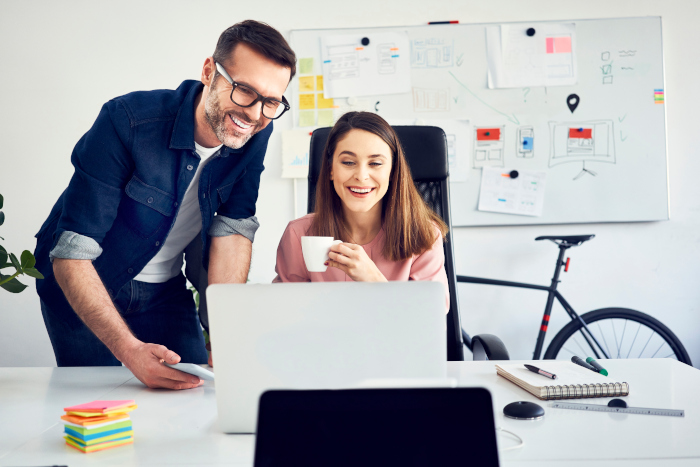 zwei Kollegen im Büro am Laptop lachen
