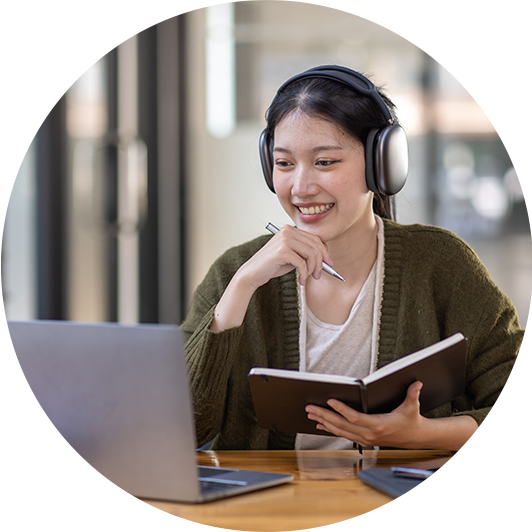 Eine junge Frau mit Notizbuch und Kopfhörern schaut sich auf dem Laptop ein Webinar über E-Commerce an.
