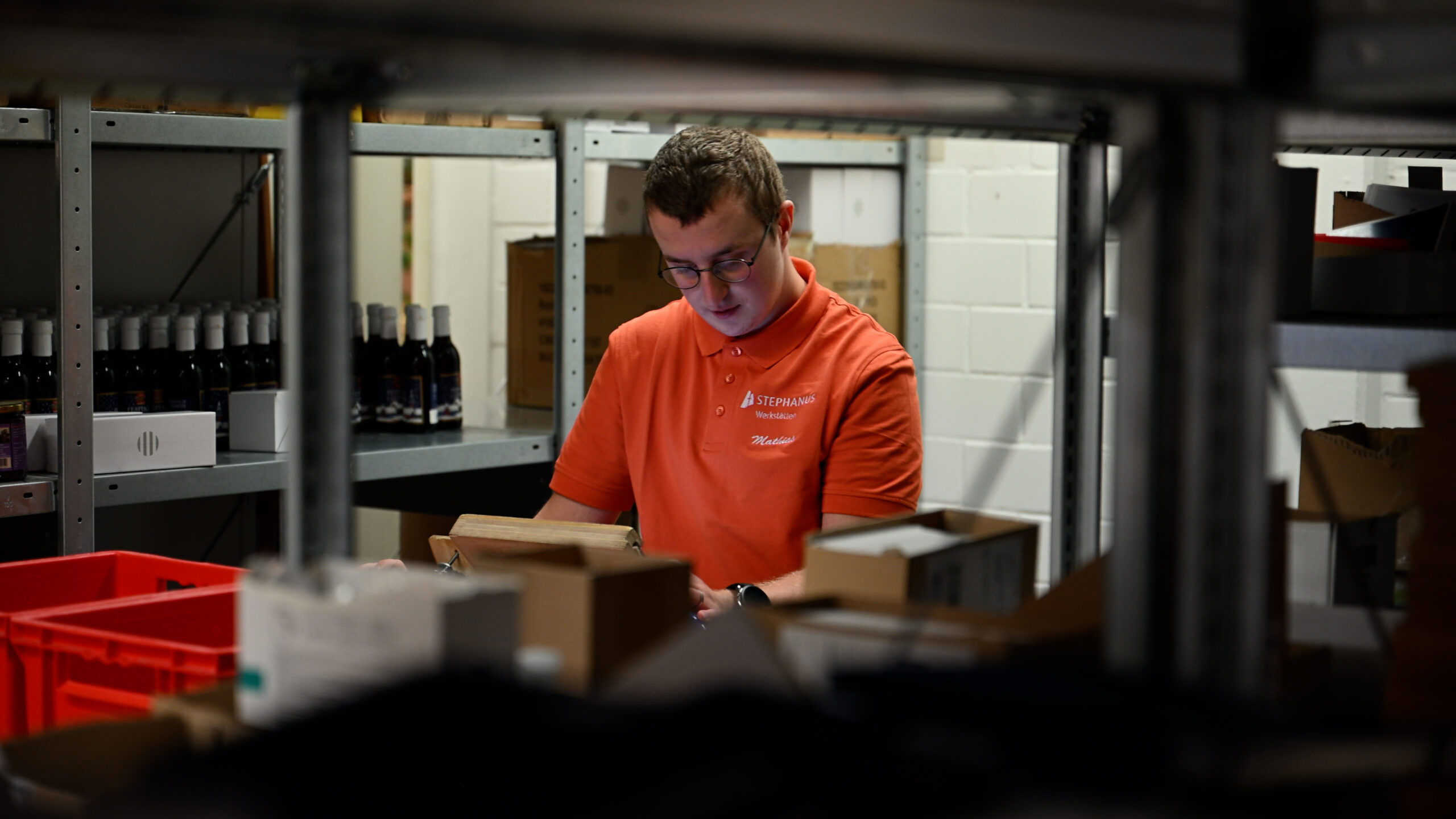 Ein Beschäftigter der Stephanus-Werkstätten konzentriert sich auf die Arbeit. Er steht zwischen Regalen und bearbeitet eine Pickliste.