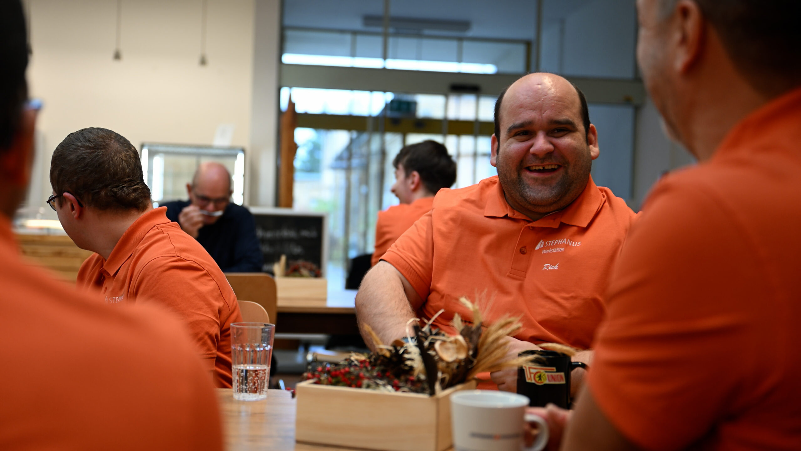 Die Beschäftigten der Stephanus-Werkstätten sitzen an den Tischen im Pausenraum und unterhalten sich.