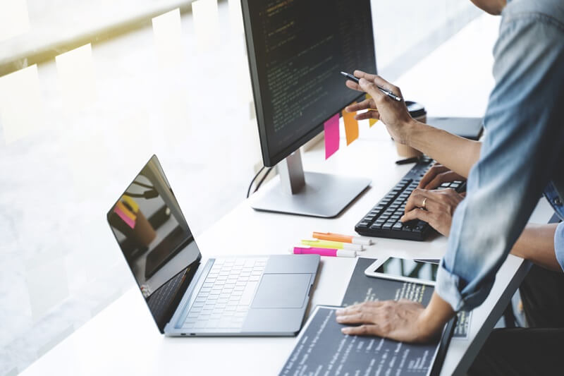 Website-Betreiber besprechen vor einem Laptop und PC-Monitor technische Strategien für nachhaltige Suchmaschinenoptimierung.