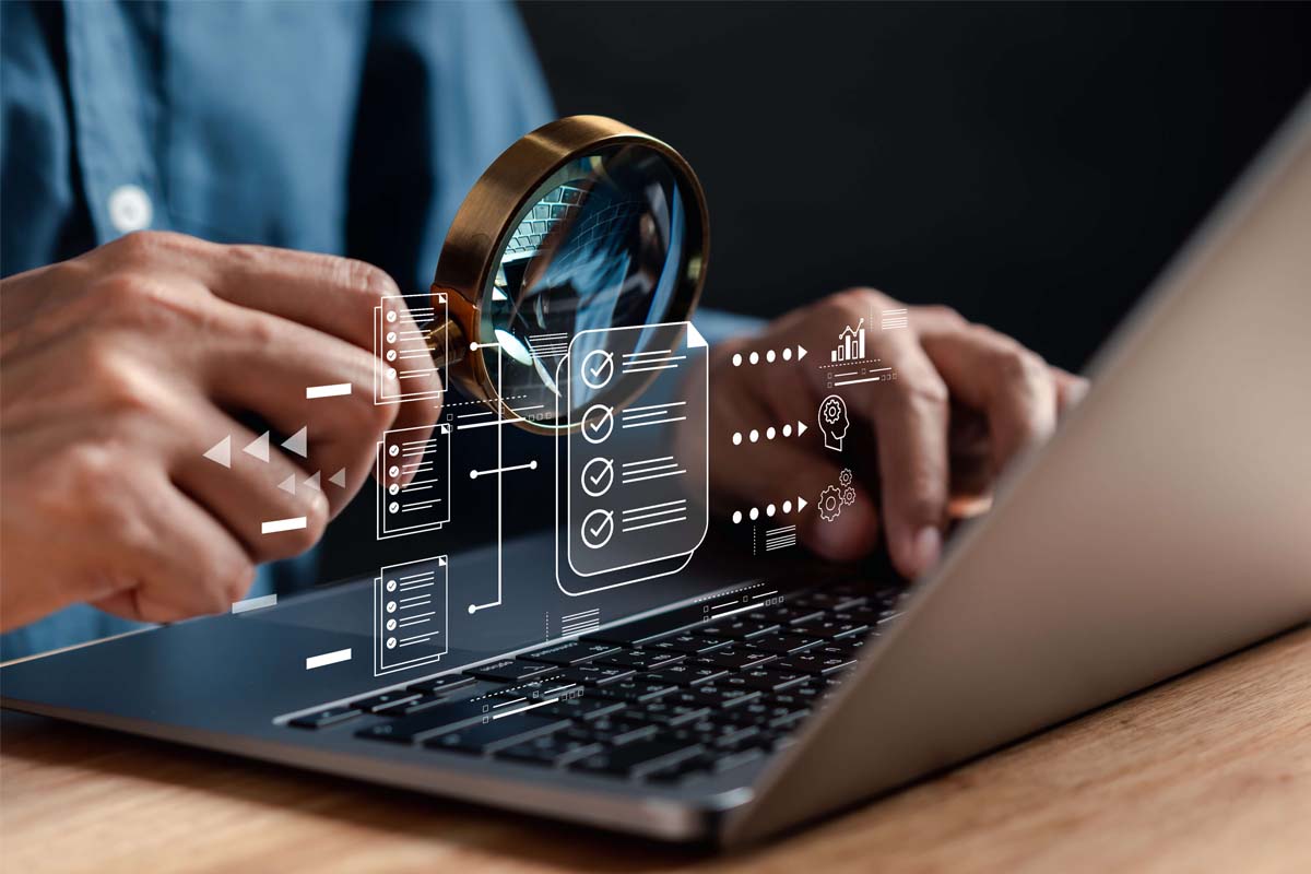 Eine Person sitzt vor einem Laptop. In ihrer rechten Hand hält sie eine Lupe. Untersucht wird eine Grafik, die Datenqualität dokumentiert.