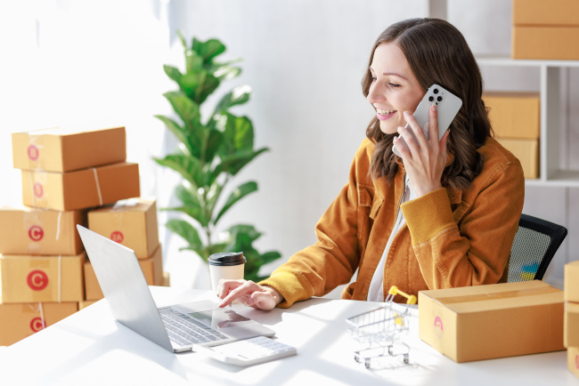 Junge Frau am Schreibtisch mit Laptop und Versandboxen