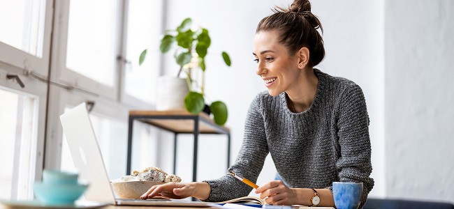 Junge Frau sitzt lächelnd am Laptop