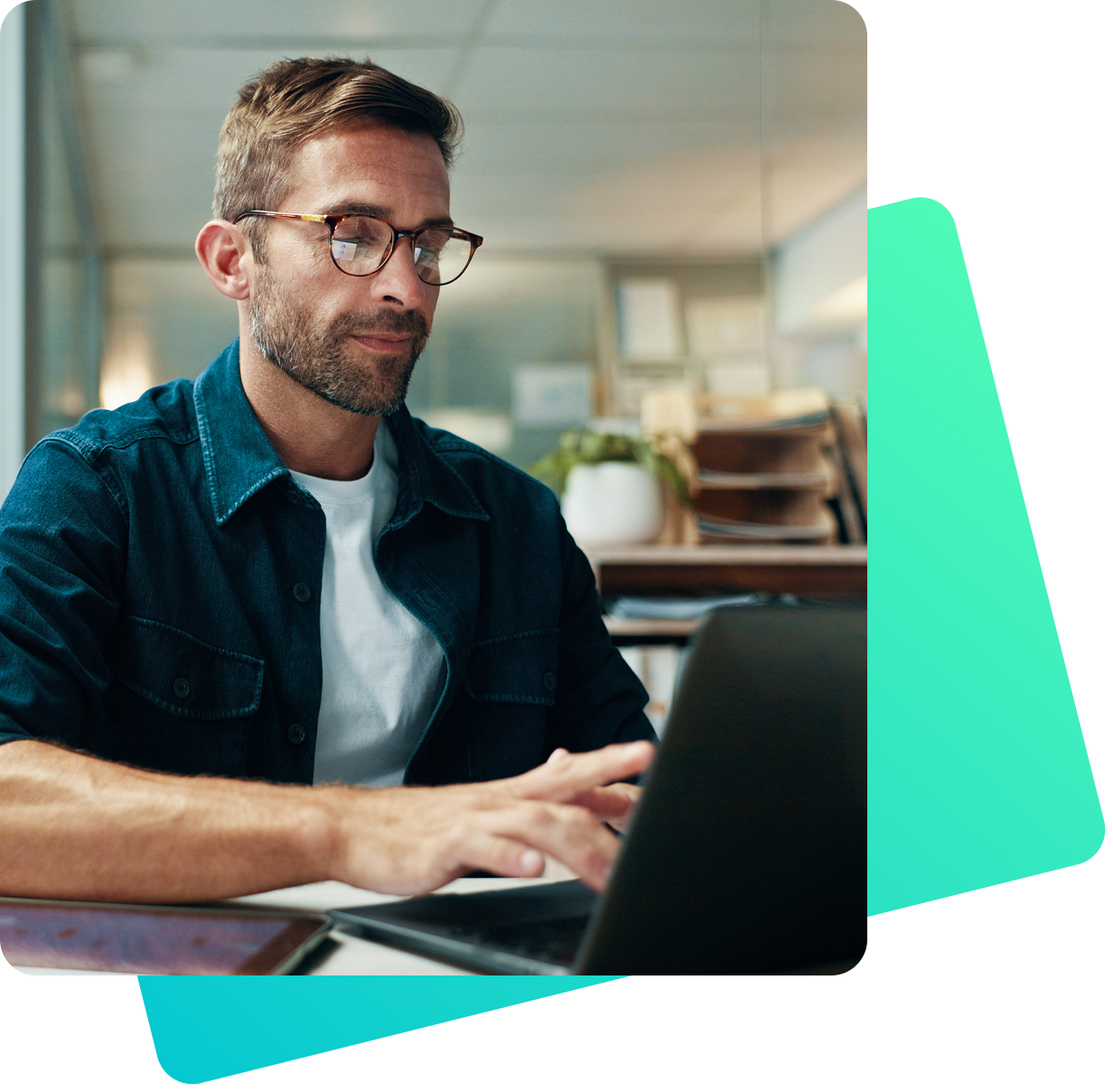 Ein Mann mit Brille und Bart arbeitet konzentriert an einem Laptop. Er trägt ein dunkelblaues Hemd über einem weißen T-Shirt. Im Hintergrund ist ein modern eingerichtetes Büro mit Pflanzen und Aktenregalen zu sehen.