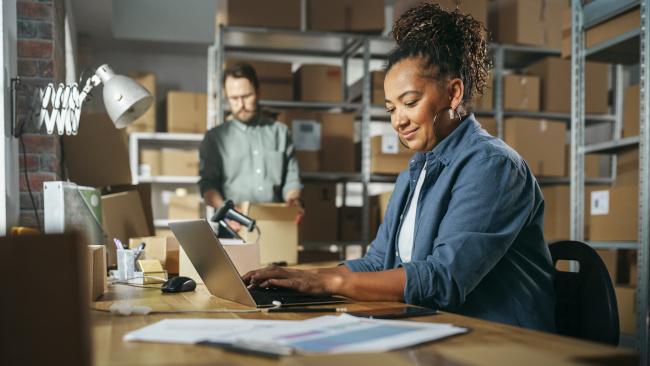 Junge Frau am Schreibtisch vor Laptop im Lager